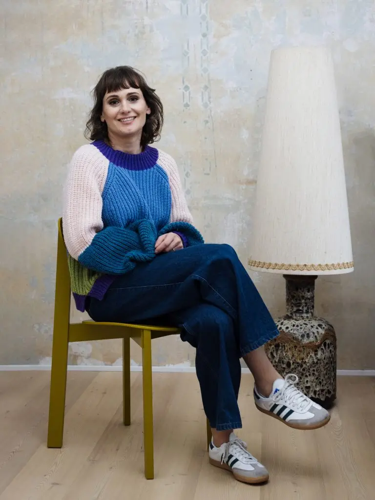 Stephanie Loy, Innenarchitektin München, sitzt lächelnd auf einem Stuhl